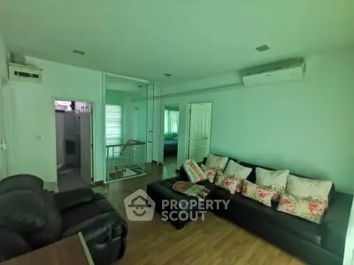 Spacious living room with modern furniture and air conditioning, featuring a cozy seating area and wooden flooring.