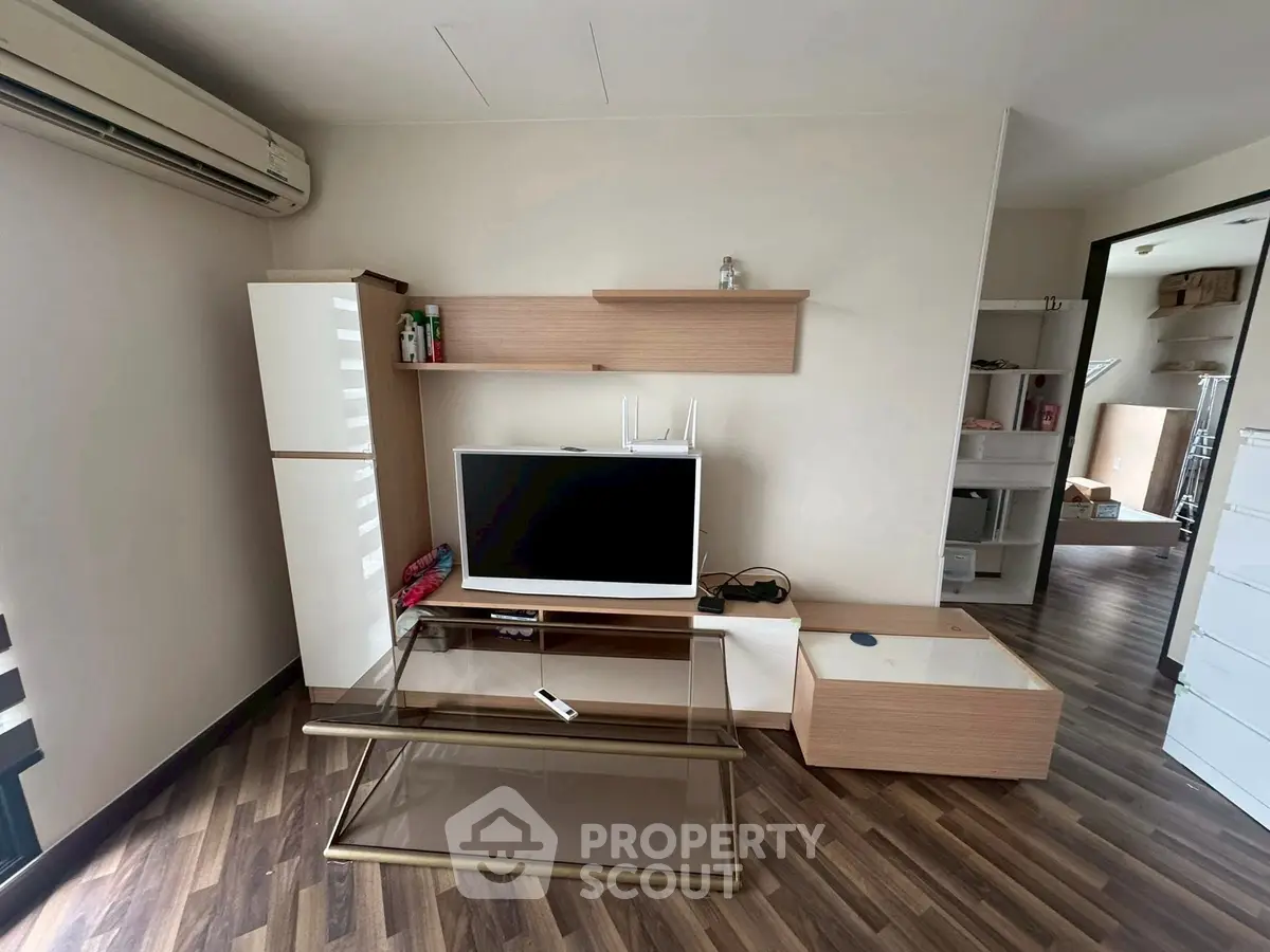 Modern living room with sleek furniture and wooden flooring, featuring a TV and stylish shelving.