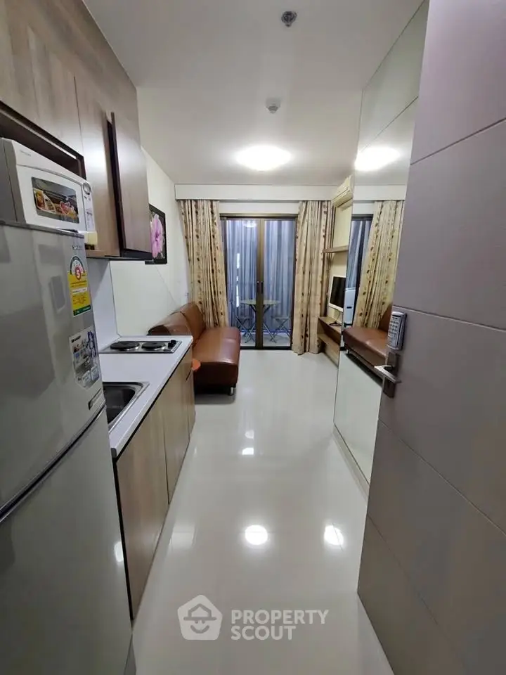 Modern apartment interior with sleek kitchen and cozy living area leading to a balcony.