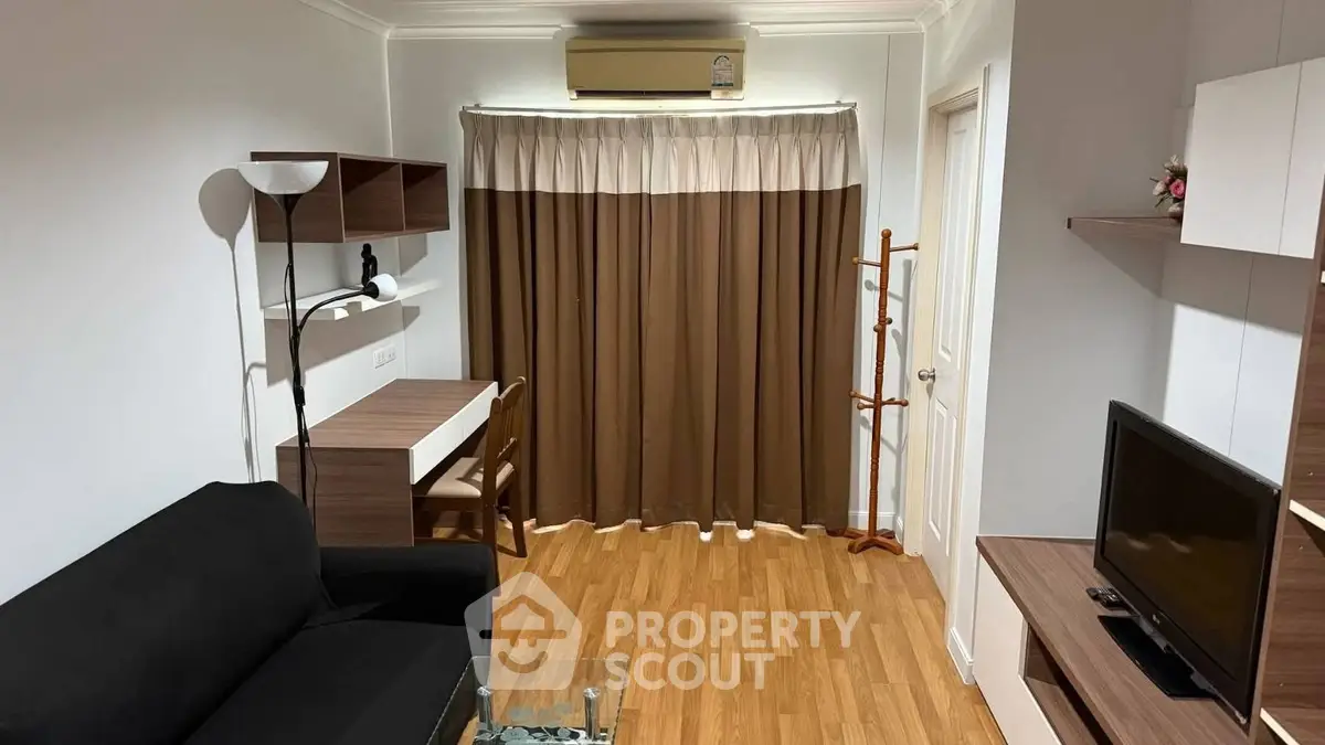 Cozy living room with modern furniture and wooden flooring, featuring a TV and air conditioning.
