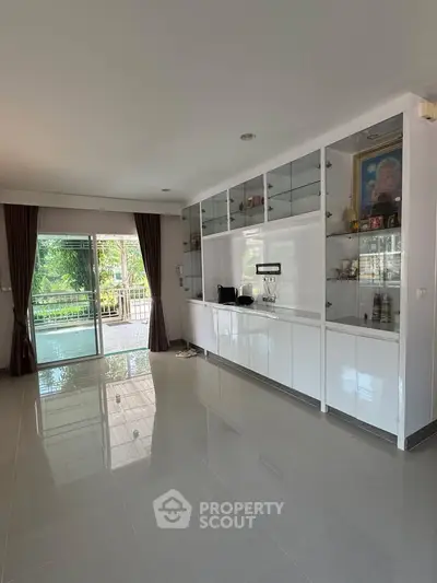 Spacious living room with sleek built-in cabinets and large sliding glass doors opening to a lush garden view.