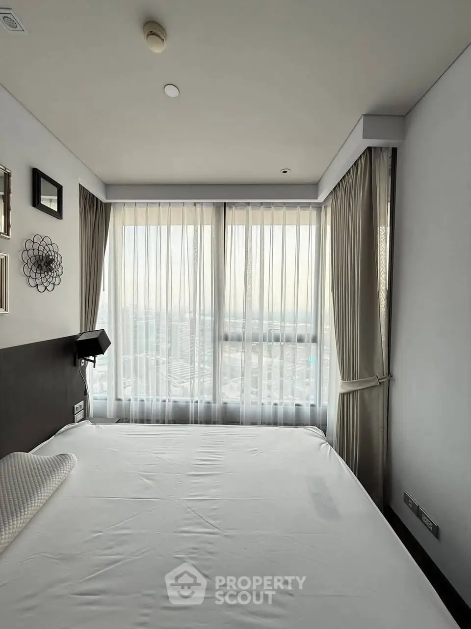 Modern bedroom with large windows and city view, featuring elegant curtains and minimalist decor.