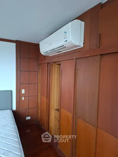 Spacious bedroom with wooden paneling and air conditioning unit, perfect for comfort and style.