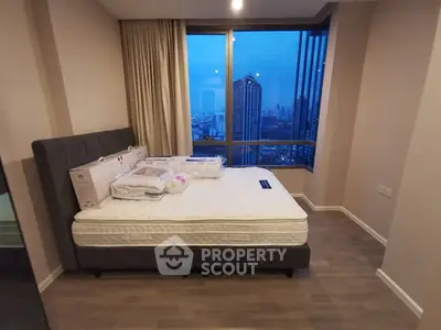 Modern bedroom with city view, featuring a new mattress and large windows in a high-rise apartment.