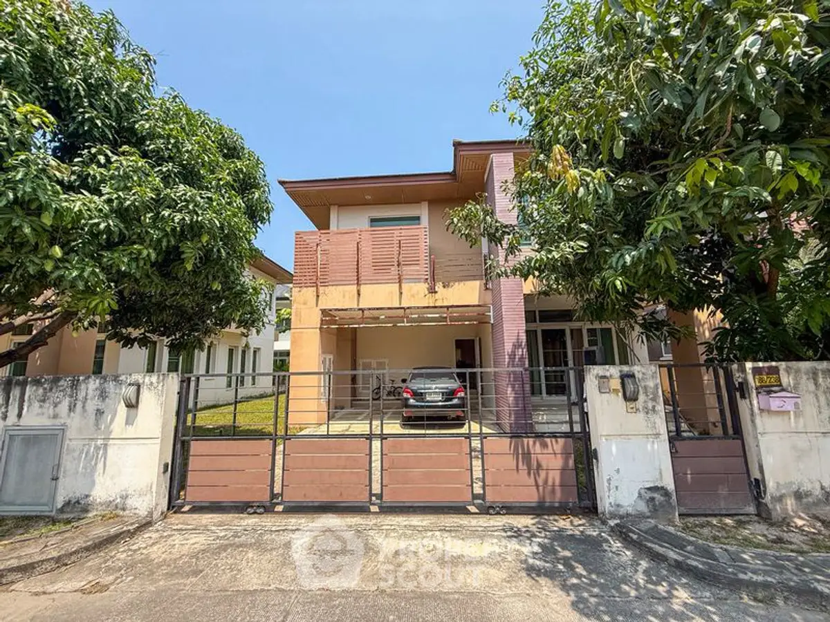 Charming two-story house with gated driveway and lush trees in a serene neighborhood.