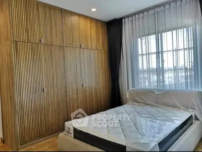 Modern bedroom with wooden paneling and large window, featuring a new mattress and sleek design.