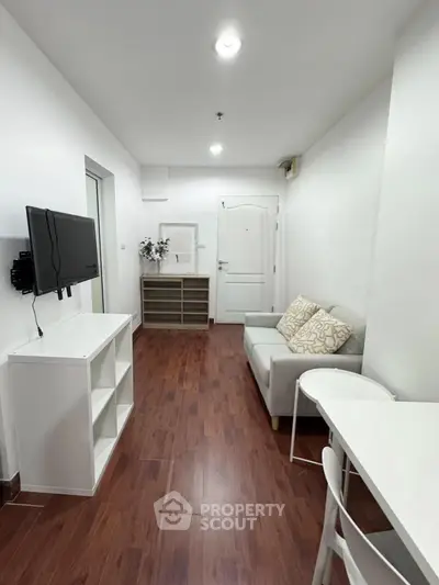 Modern living room with wooden flooring, white furniture, and wall-mounted TV in a cozy apartment.