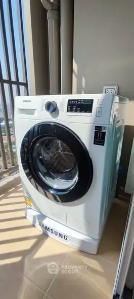 Modern Samsung washing machine on a sunny balcony with city view.