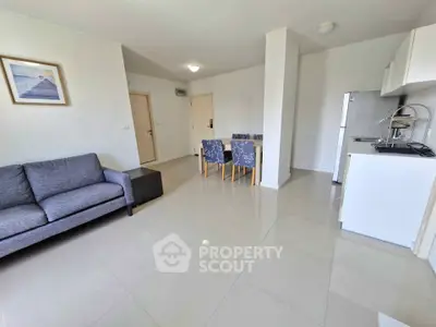 Modern open-plan living room with sleek kitchen and dining area, featuring stylish furniture and bright lighting.