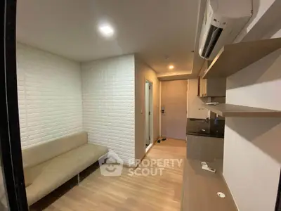 Modern compact living room with sleek wooden flooring and built-in shelves, featuring a cozy sofa and air conditioning.