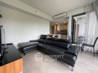 Modern living room with sleek black leather sofa and open kitchen layout in a stylish apartment.