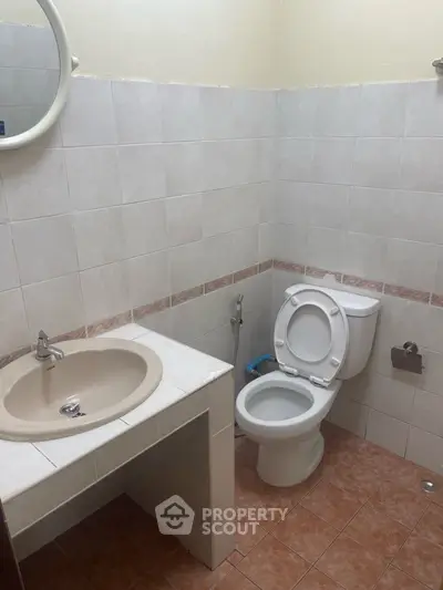 Compact bathroom with tiled walls and floor, featuring a toilet and sink.
