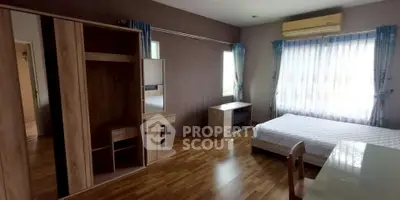 Spacious bedroom with wooden flooring and modern furniture, featuring large windows and natural light.