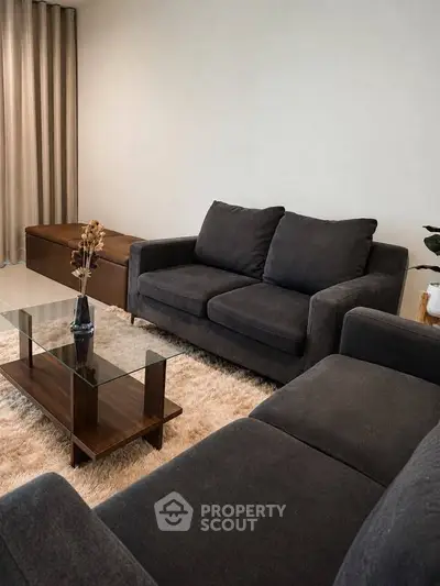 Elegant living room with plush dark sofas and modern glass coffee table on a cozy rug.