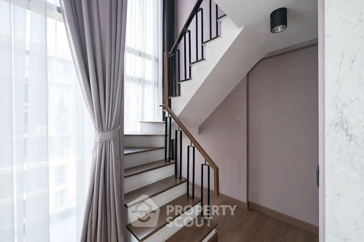 Elegant staircase with modern railing and natural light in a stylish home interior.