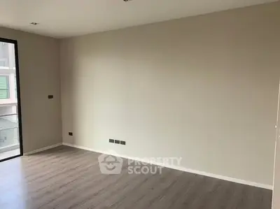Spacious empty room with wooden flooring and large window in modern apartment.