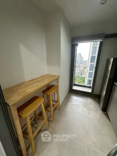 Modern kitchen with tall wooden table and stools, offering a city view through large window.