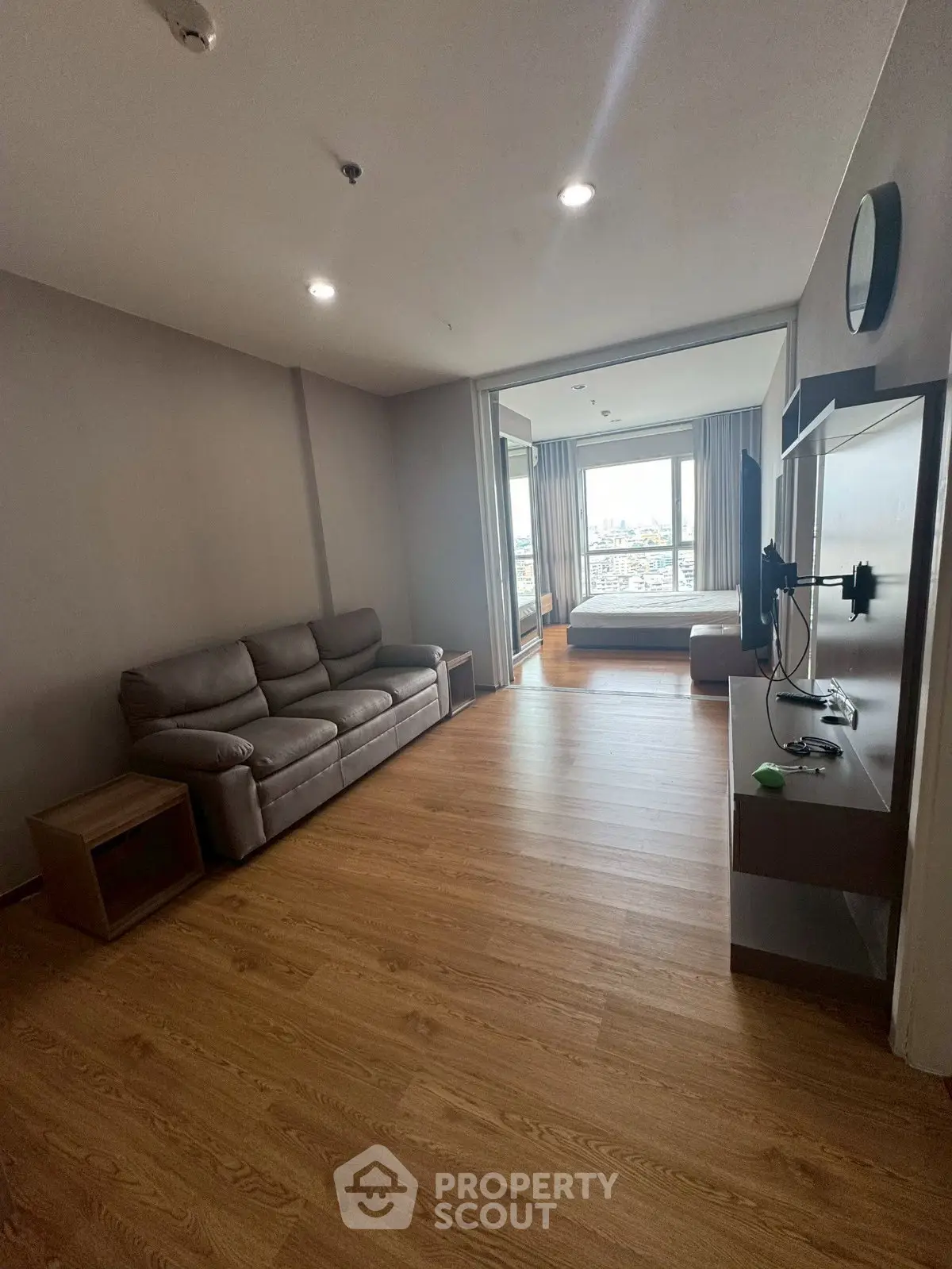 Spacious living room with wooden flooring and modern furnishings, featuring a large window with city view.