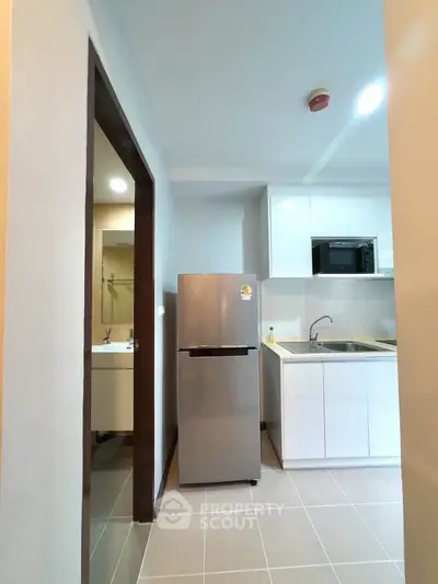 Modern kitchen with sleek white cabinets and stainless steel fridge in a compact layout.