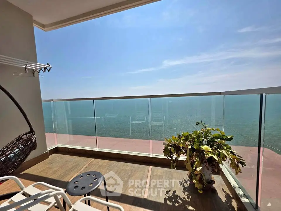 Stunning ocean view from a spacious balcony with glass railing and cozy seating area.