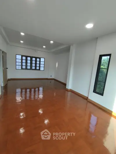 Spacious empty room with polished wooden floors and large windows, ideal for customization.