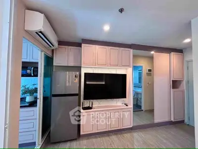 Modern living room with sleek cabinetry and large TV, featuring stylish pink accents and a stainless steel fridge.