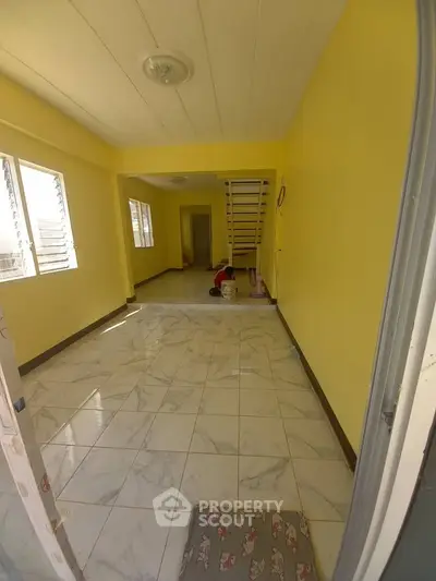 Spacious yellow-walled room with tiled flooring and staircase, ideal for versatile living space.
