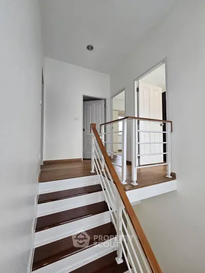 Modern staircase with wooden steps and white railings in a bright, minimalist home interior.