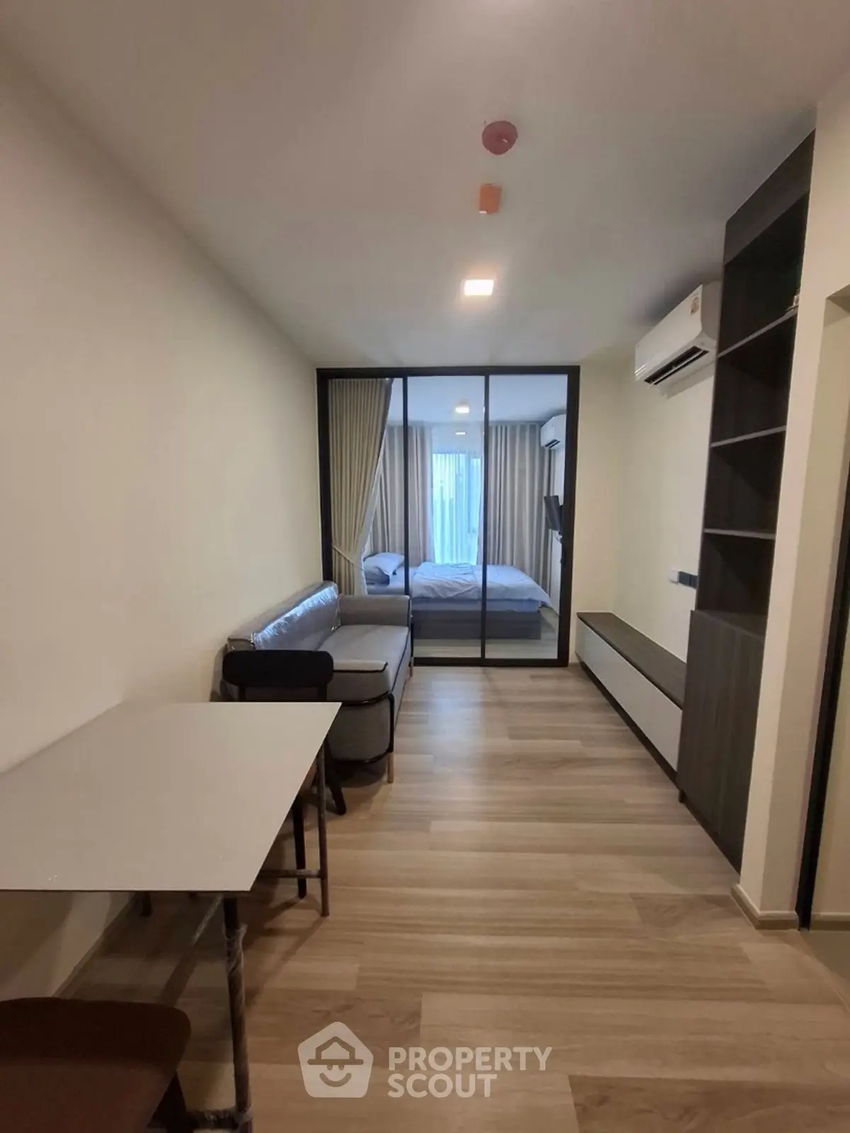 Modern apartment interior with open living room and bedroom layout, featuring sleek furniture and wooden flooring.