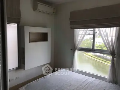 Cozy bedroom with large window offering serene river view, featuring air conditioning and modern design.