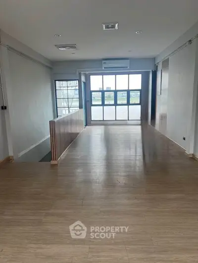 Spacious open-plan room with large windows and wooden flooring, ideal for versatile use.