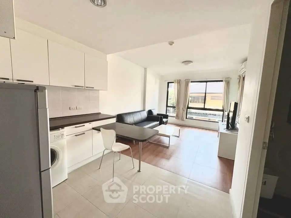 Modern open-plan living room with kitchen, featuring sleek furniture and large windows for natural light.