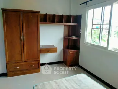 Cozy bedroom with wooden wardrobe and large window offering natural light.