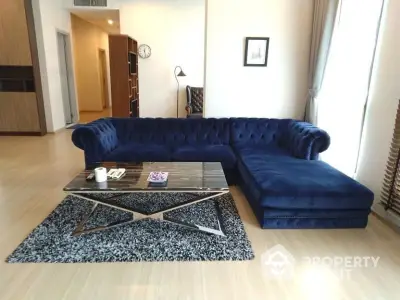 Elegant living room with plush blue sectional sofa, modern glass coffee table, and sleek wooden flooring, perfect for upscale urban living.