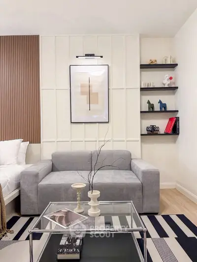 Modern living room with stylish decor, featuring a gray sofa, glass coffee table, and contemporary wall art.