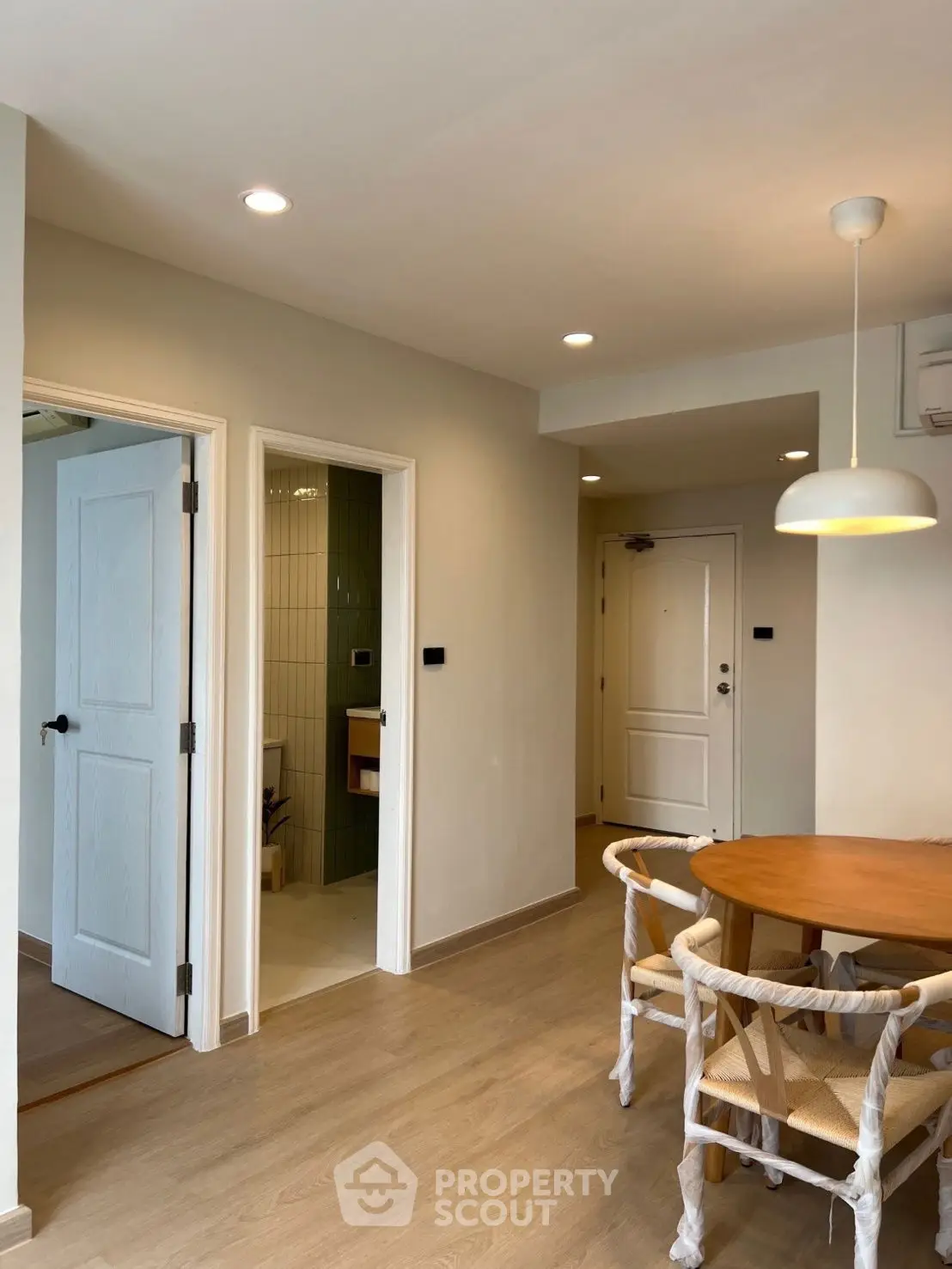 Modern dining area with wooden table and chairs, adjacent to a bathroom and entrance.