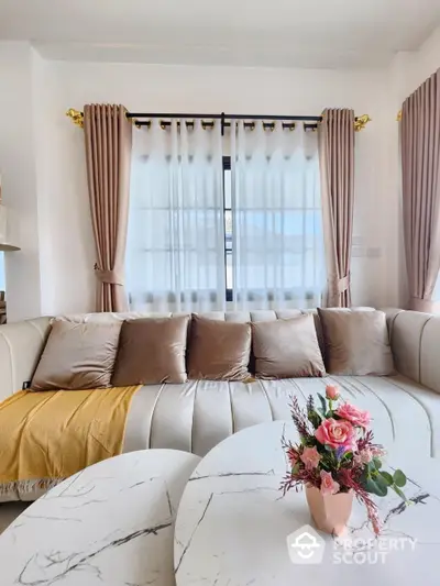 Elegant living room with plush cream sectional sofa, gold accents, and sophisticated marble coffee table, bathed in natural light from the large window.