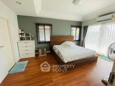 Spacious bedroom with wooden flooring and large windows for natural light.
