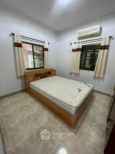 Cozy bedroom with air conditioning and natural light, featuring a comfortable bed and tiled flooring.