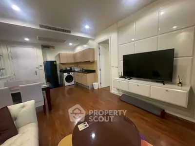 Modern living room with open kitchen, featuring hardwood floors and sleek appliances.