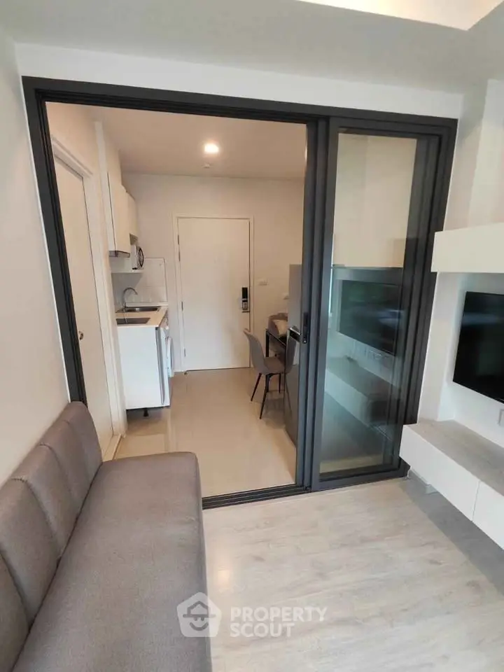 Modern apartment interior with sliding glass door separating living room and kitchen area.