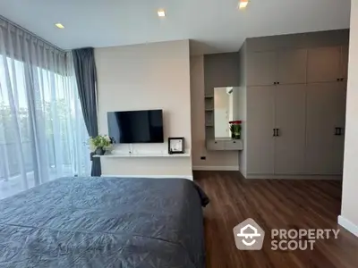 Spacious bedroom with modern design, featuring a large bed, built-in wardrobes, and a sleek entertainment unit, complemented by natural light from floor-to-ceiling windows.