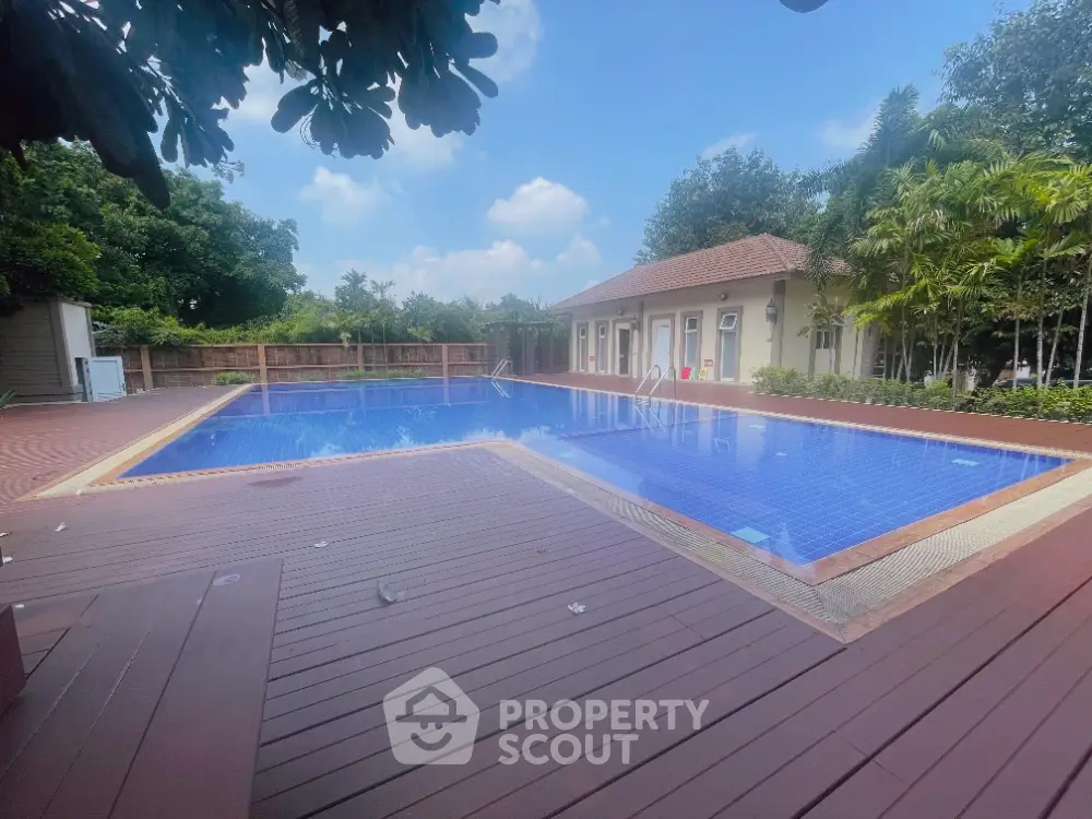 Luxurious outdoor pool area with wooden deck and lush greenery, perfect for relaxation and leisure.