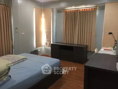 Spacious bedroom with wooden flooring and ample natural light, featuring modern furniture and cozy ambiance.