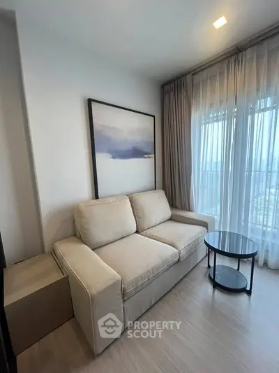 Cozy living room with modern sofa and elegant decor, featuring large windows with sheer curtains.