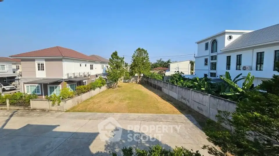 Spacious residential plot with modern houses and lush greenery, ideal for new development.