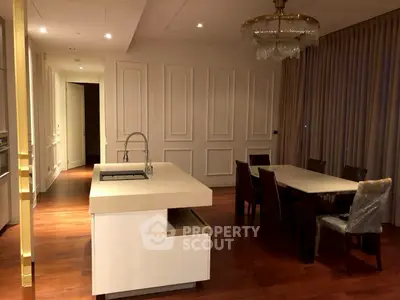 Luxurious dining area with elegant chandelier and modern kitchen island in upscale apartment.