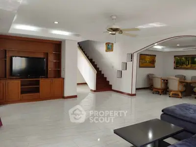 Spacious living room with modern furniture and open dining area, featuring elegant staircase.