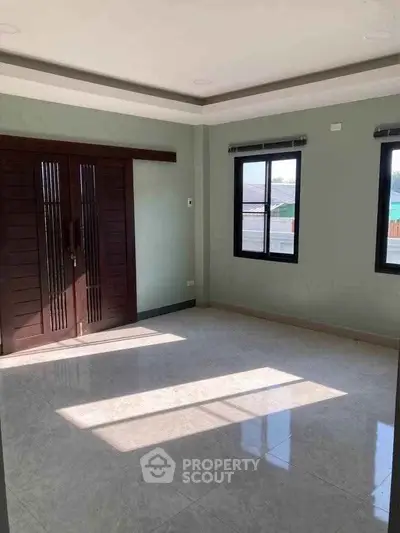 Spacious sunlit room with large windows and elegant wooden doors, perfect for versatile living space.