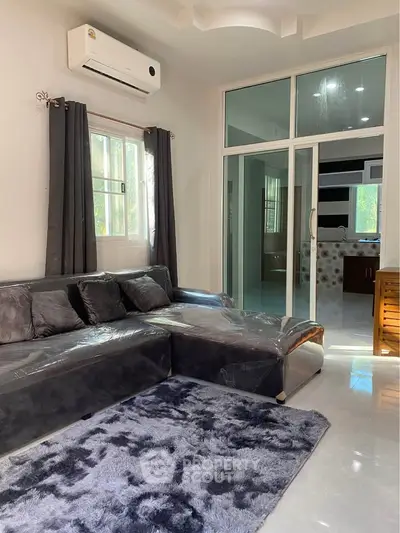 Spacious living room with modern sofa and plush rug, featuring large windows and sliding glass doors.